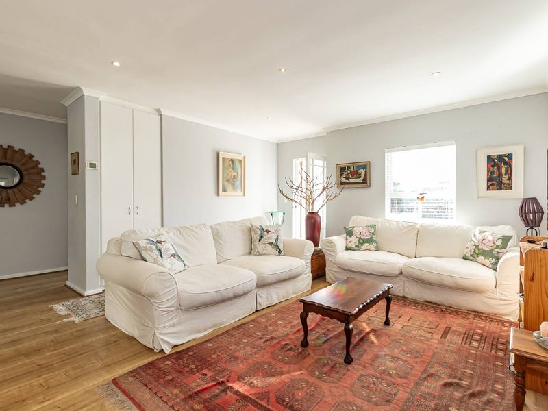 A bright and well-maintained living room featuring laminate flooring, recessed downlights, and a built-in storage cupboard.