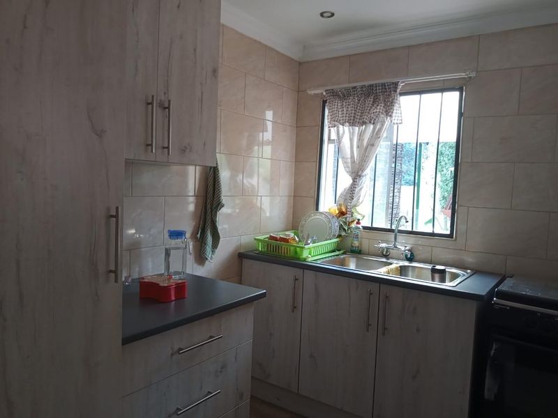 A functional kitchen featuring wood-look laminate cabinetry, dark countertops, a stainless steel double sink, and tiled wall finishes with natural light.