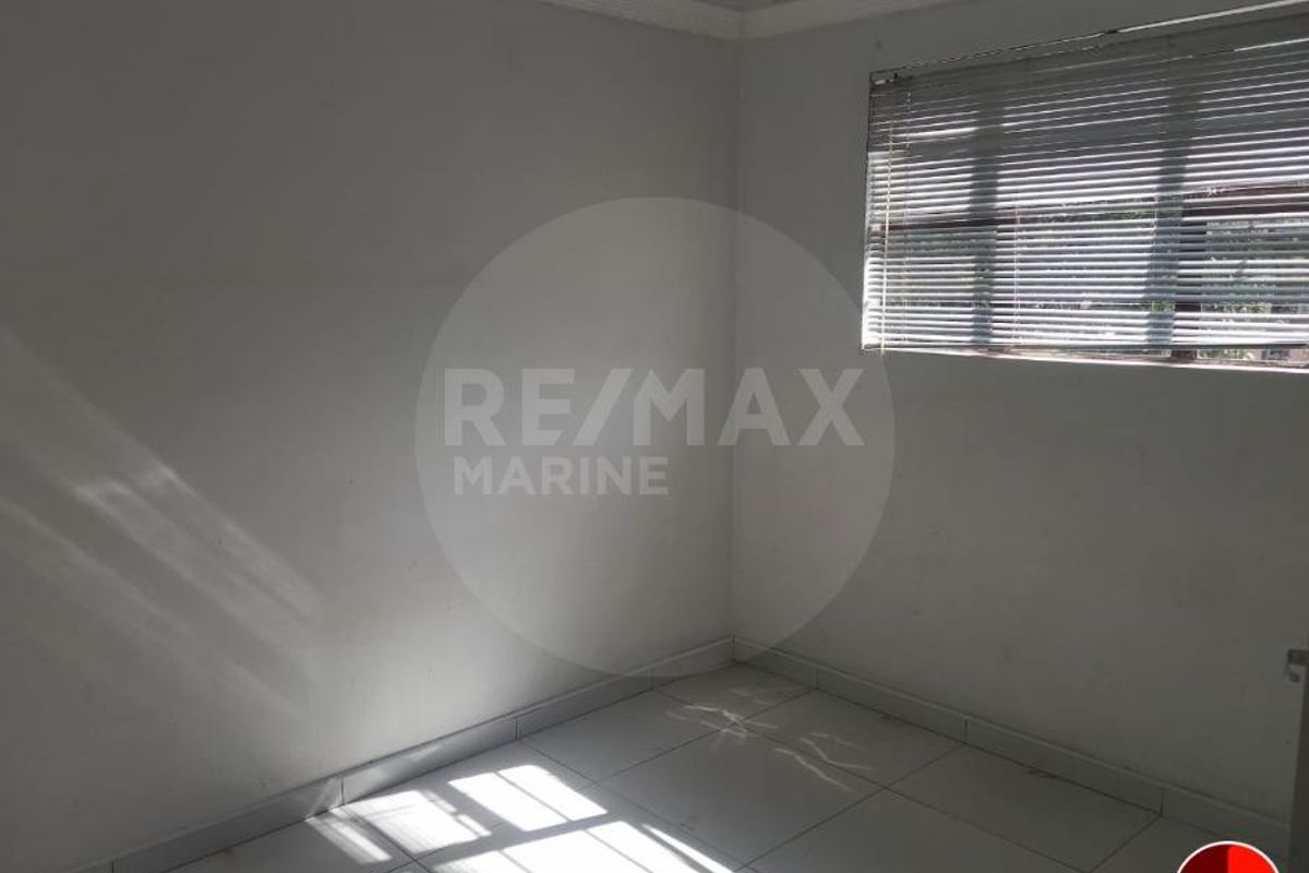 An empty bedroom featuring tiled flooring, a window with fitted blinds, and plain walls, offering a blank canvas for personalization.