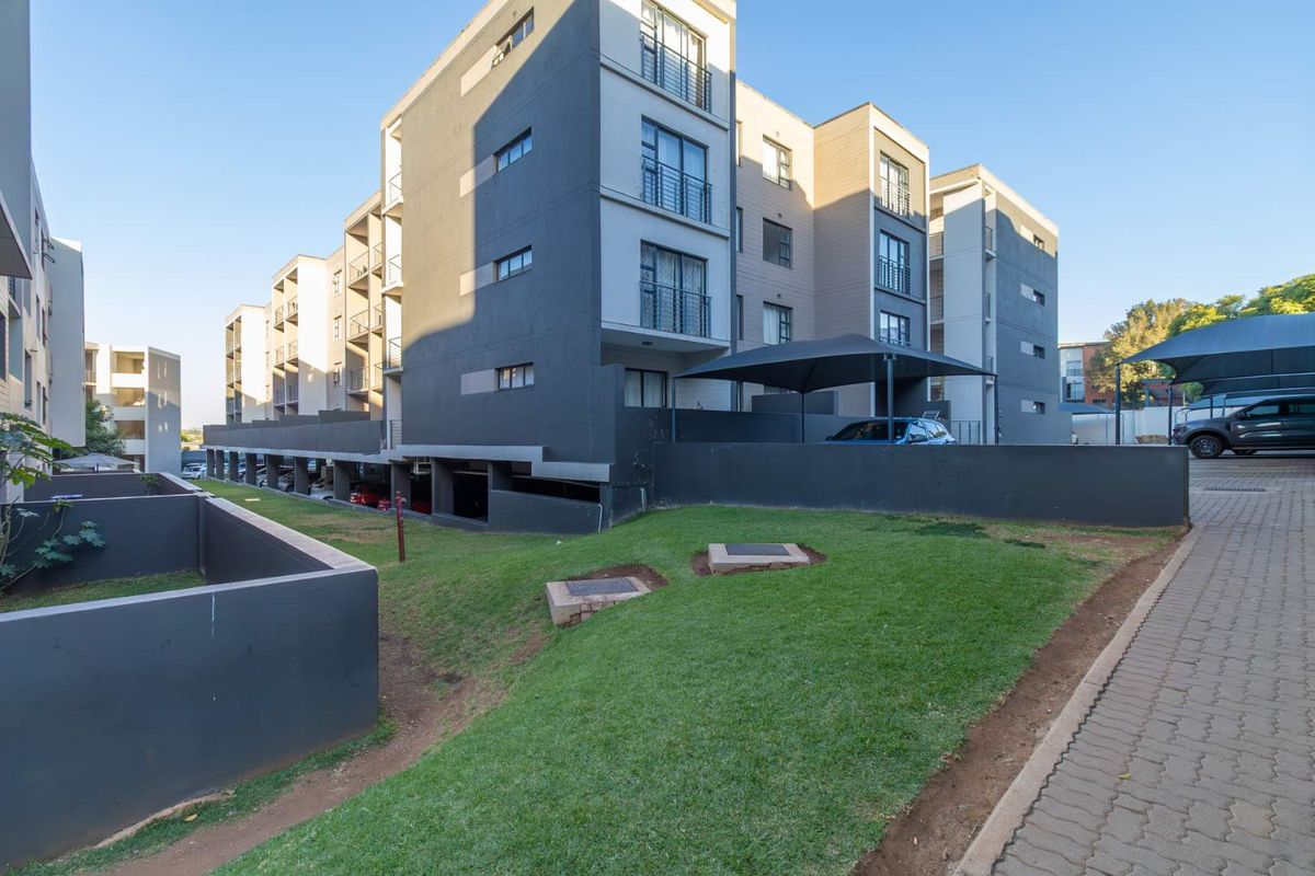 Exterior view of a modern apartment complex featuring landscaped lawn areas, paved walkways, and covered parking bays.