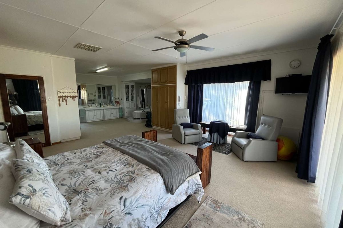 Spacious primary bedroom suite featuring an integrated open-plan bathroom area, built-in wooden cabinetry, and a ceiling fan.