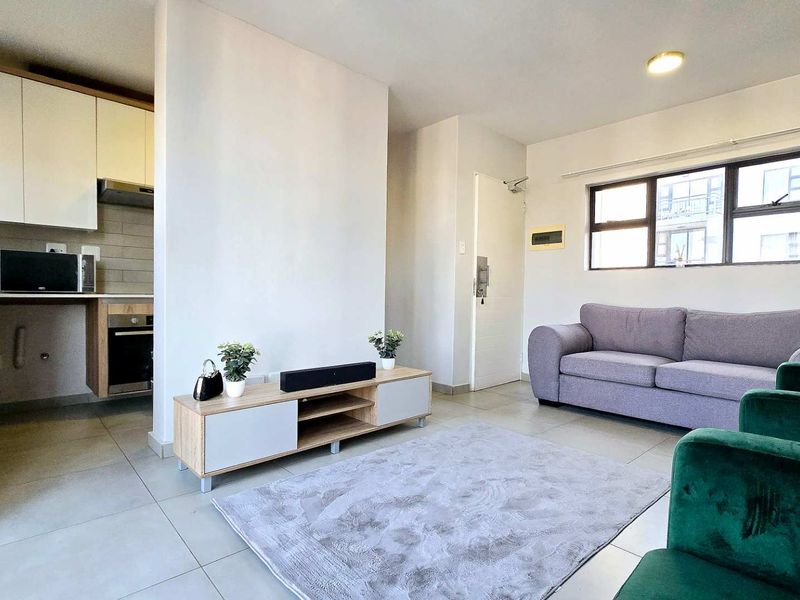 Open-plan living area featuring tiled flooring, a modern kitchen with built-in cabinetry and appliances, and large windows providing natural light.