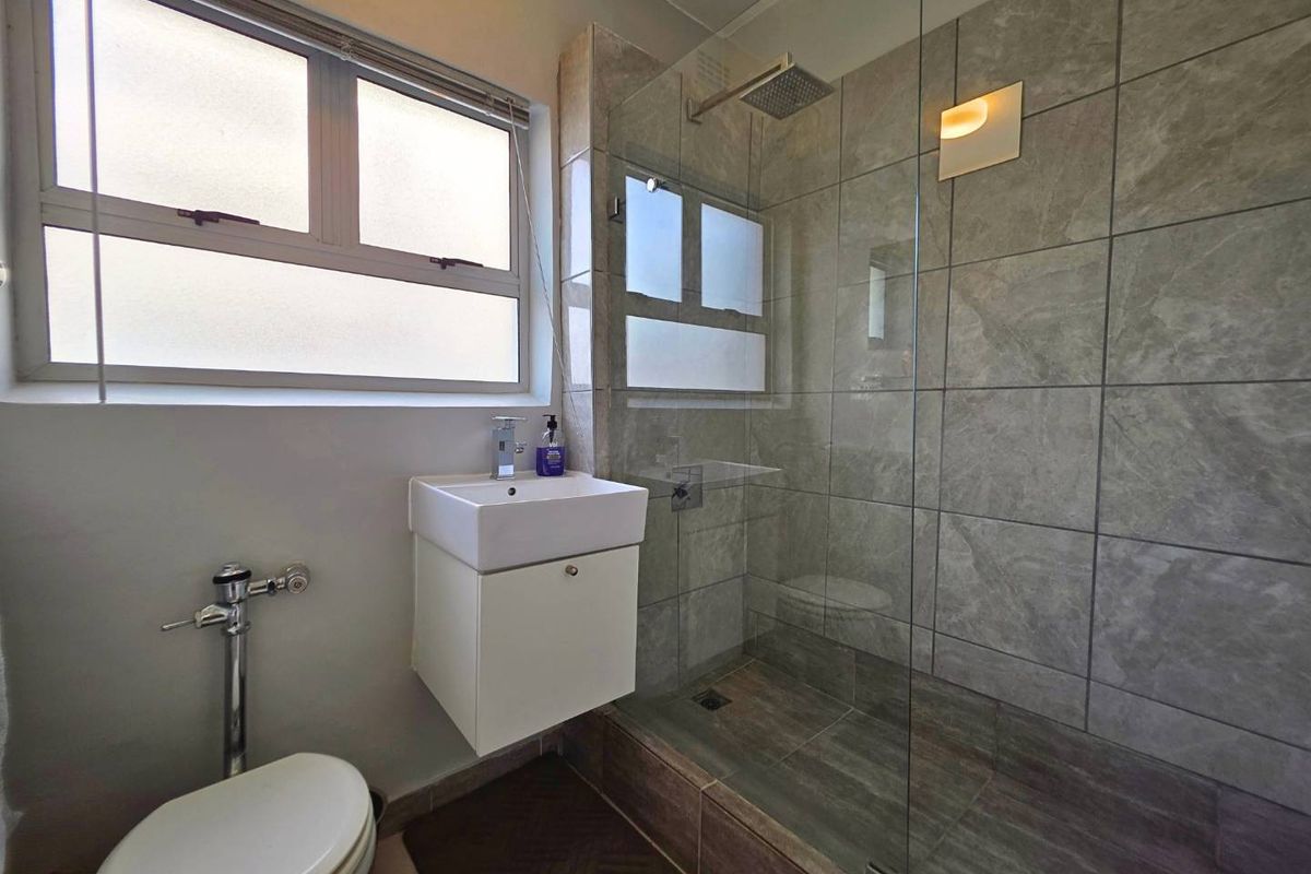 Modern bathroom featuring a glass-enclosed shower with rain shower head, wall-mounted vanity, and neutral grey tiling throughout.
