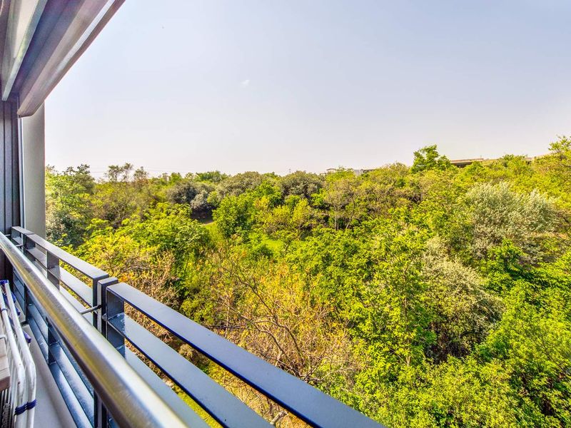 A private balcony featuring a metal balustrade and tiled flooring, offering an elevated view of the surrounding lush green trees.