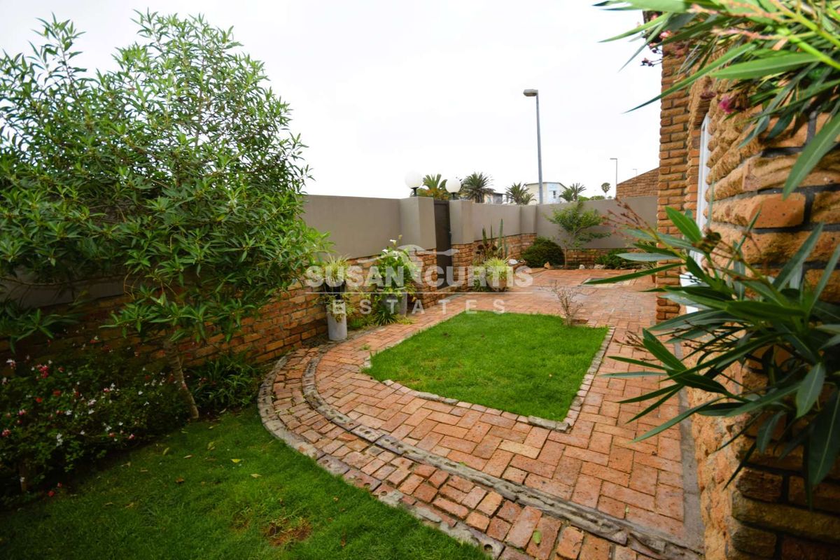 A private rear garden featuring a brick-paved patio area with a small central lawn, enclosed by brick boundary walls.
