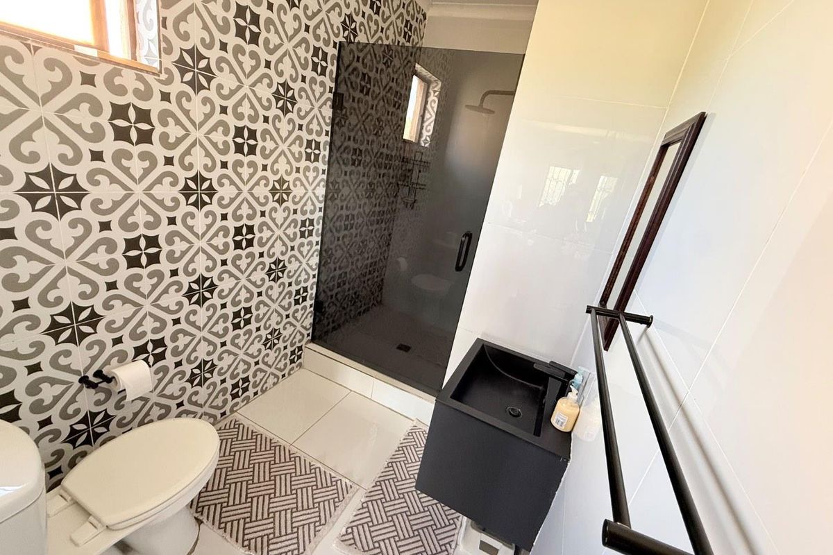 Modern bathroom featuring a walk-in shower with dark glass enclosure, patterned feature tiling, and a contemporary black wall-mounted vanity basin.