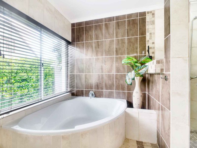 A bright bathroom featuring a built-in corner bathtub, a separate shower enclosure, and neutral tiled finishes throughout.