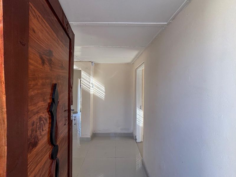 A bright, empty hallway featuring tiled flooring and a solid timber entrance door, providing access to the interior living spaces.