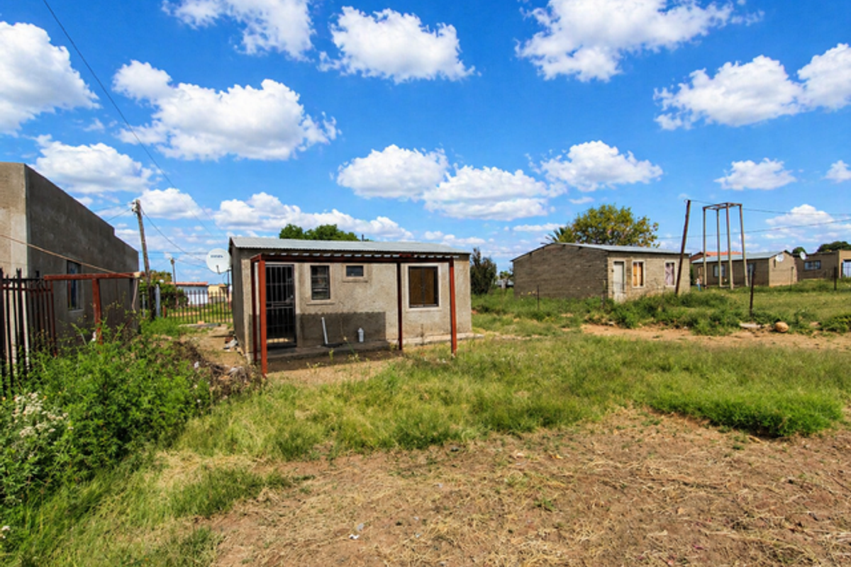 A detached single-story dwelling featuring a simple structure with a metal roof, set on a large, undeveloped plot of land.