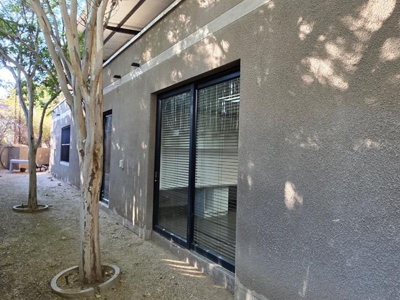 Rear exterior view of the office building featuring a textured stucco facade, sliding glass doors, and a corrugated metal roof structure.