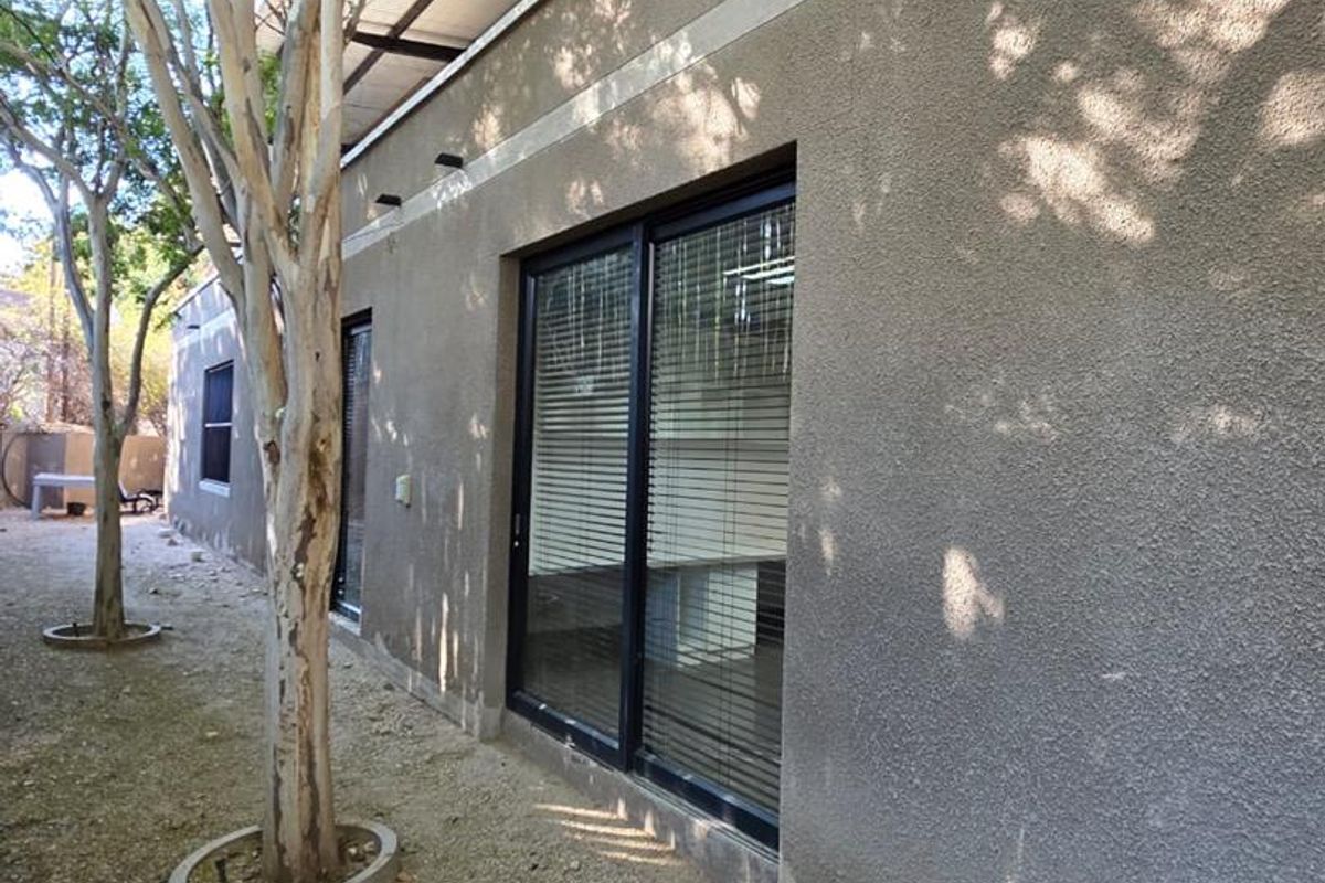 Rear exterior view of the office building featuring a textured stucco facade, sliding glass doors, and a corrugated metal roof structure.