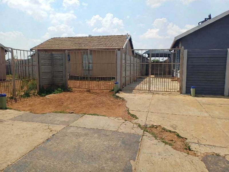 Rear exterior view showing a concrete driveway, metal security gates, and precast boundary walling surrounding the property.