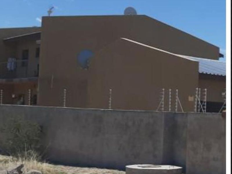 Exterior view of the apartment complex featuring a perimeter wall with electric fencing and a satellite dish mounted on the roof.