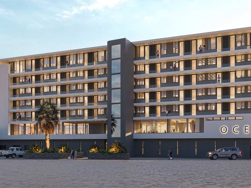 A modern multi-story apartment building facade featuring private balconies with glass balustrades, located directly on the beachfront.