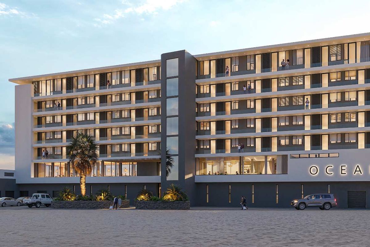 A modern multi-story apartment building facade featuring private balconies with glass balustrades, located directly on the beachfront.