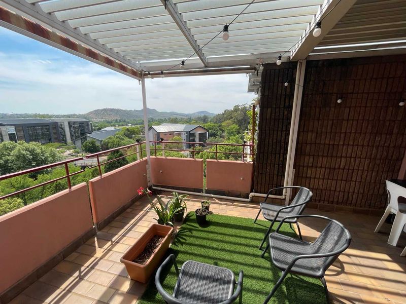 A covered balcony featuring a louvred pergola, tiled flooring, and a metal balustrade, offering elevated views of the surrounding area.