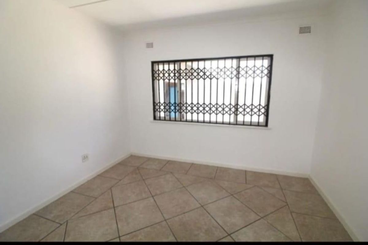 A clean, empty bedroom featuring neutral tiled flooring and a window fitted with a security gate.