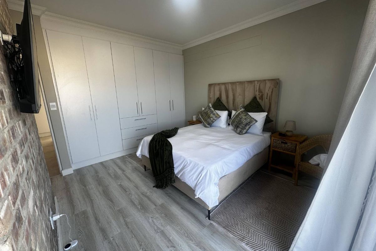 A well-maintained bedroom featuring built-in floor-to-ceiling wardrobes, modern wood-look laminate flooring, and a feature brick wall.