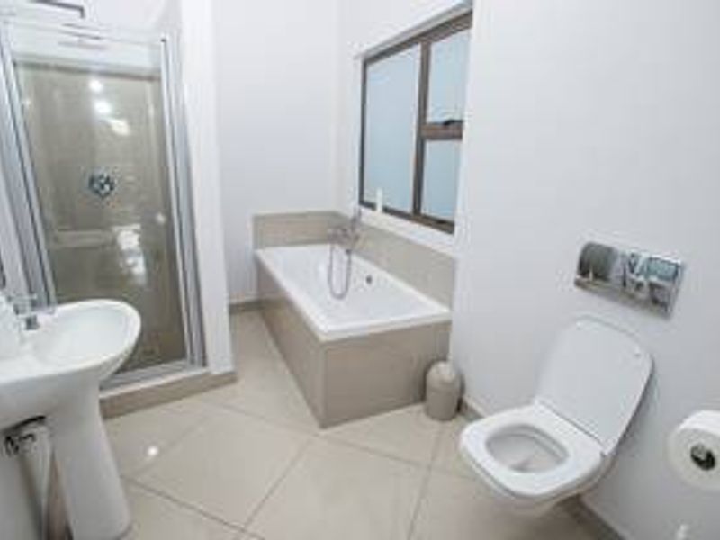 Modern bathroom featuring a pedestal basin, glass shower enclosure, built-in bathtub, and wall-mounted toilet with neutral tiled flooring.