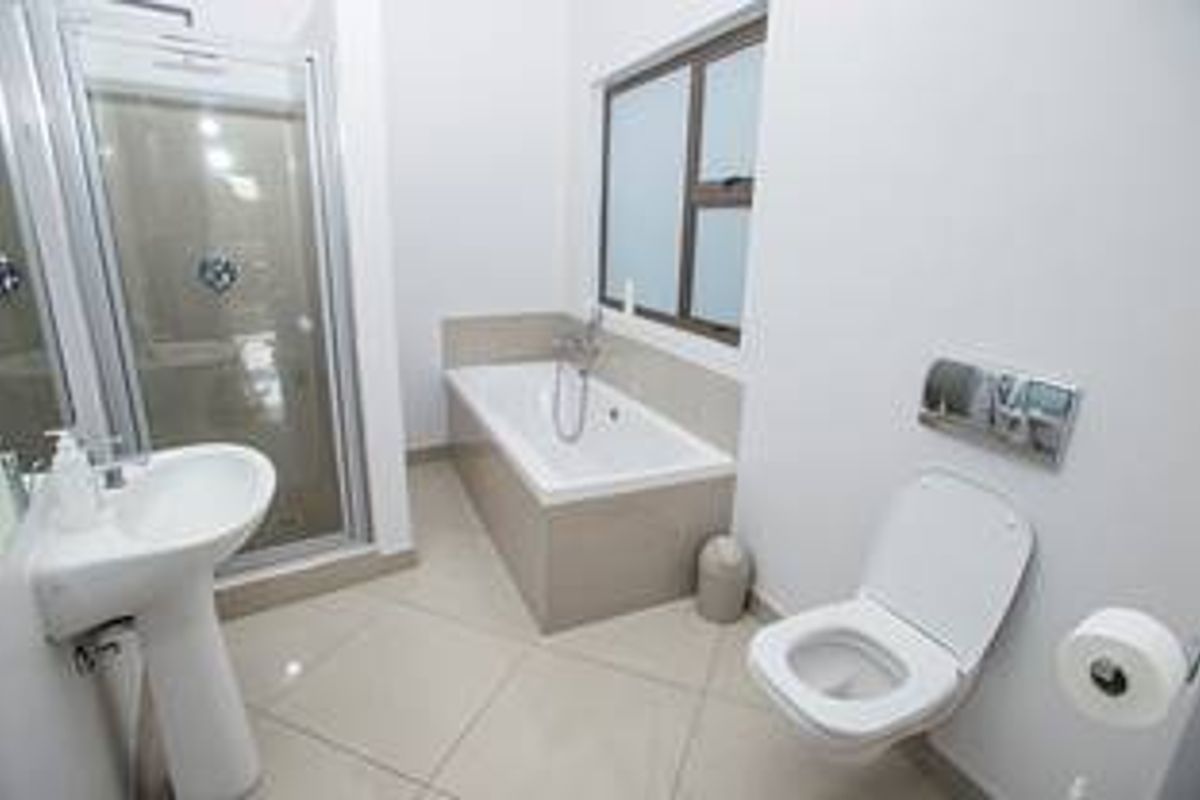 Modern bathroom featuring a pedestal basin, glass shower enclosure, built-in bathtub, and wall-mounted toilet with neutral tiled flooring.