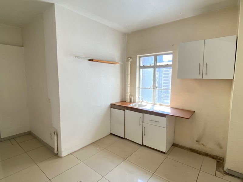 A compact, empty kitchen area featuring basic cabinetry, a sink, and tiled flooring, requiring cosmetic updates and repairs to the wall finishes.