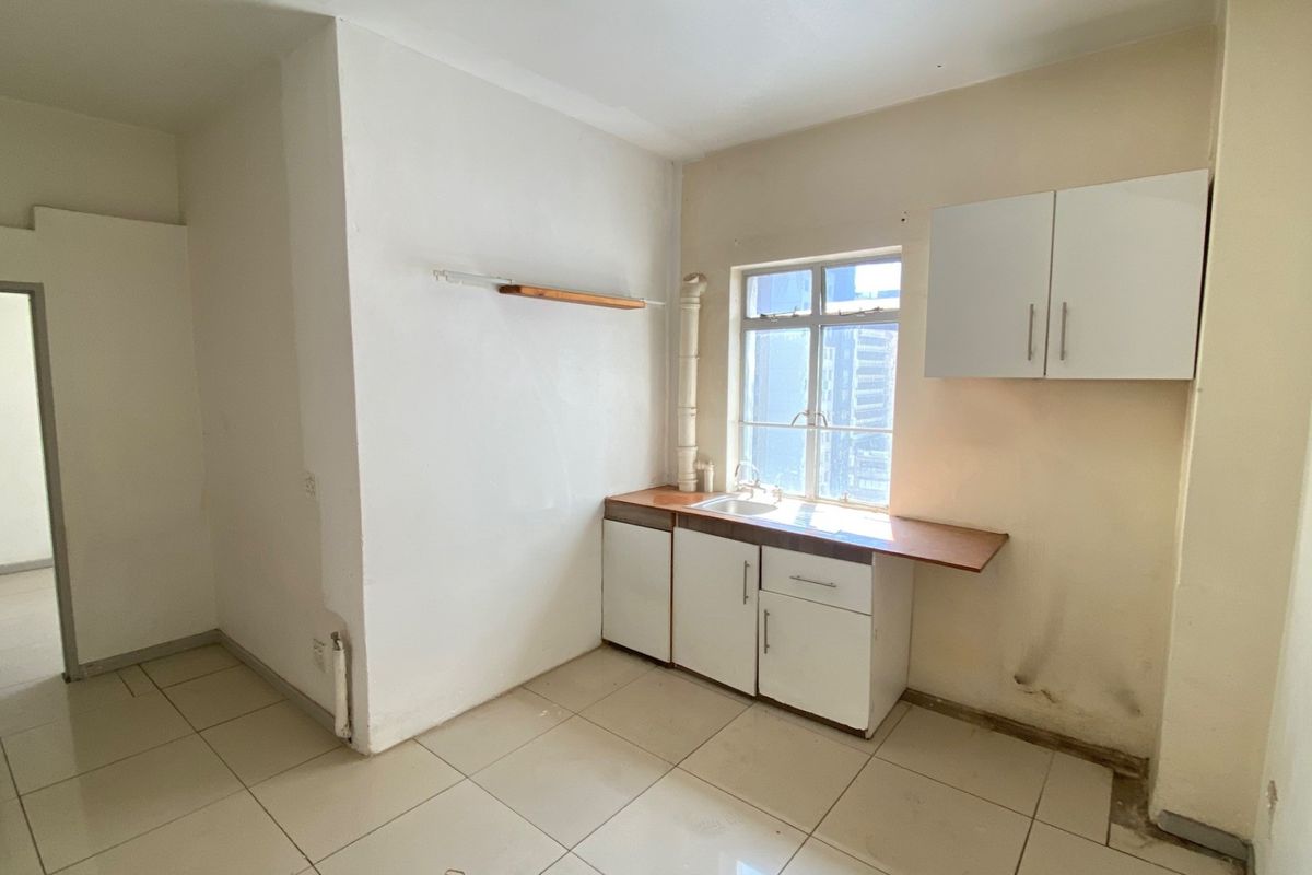 A compact, empty kitchen area featuring basic cabinetry, a sink, and tiled flooring, requiring cosmetic updates and repairs to the wall finishes.
