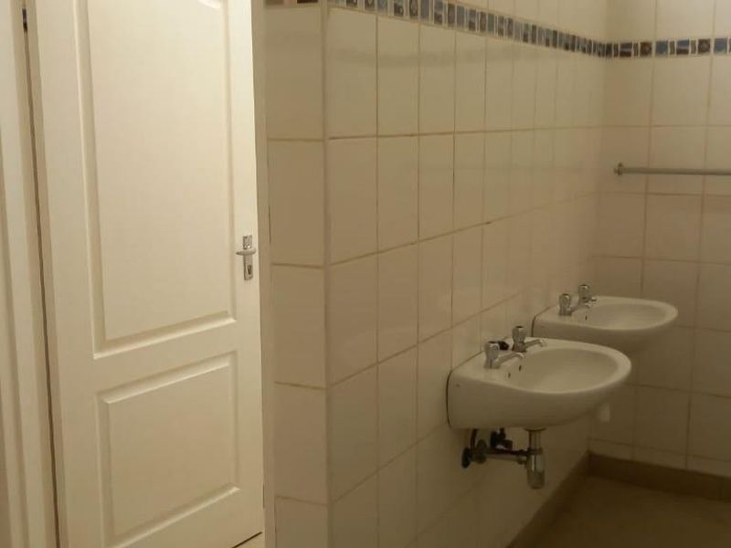 A functional bathroom space featuring dual wall-mounted ceramic basins and tiled wall finishes, presenting a clean but dated aesthetic.