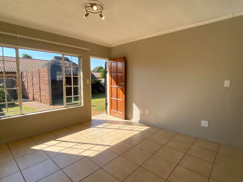 An empty living room featuring tiled flooring, a large window, and direct access to the garden through a timber door.