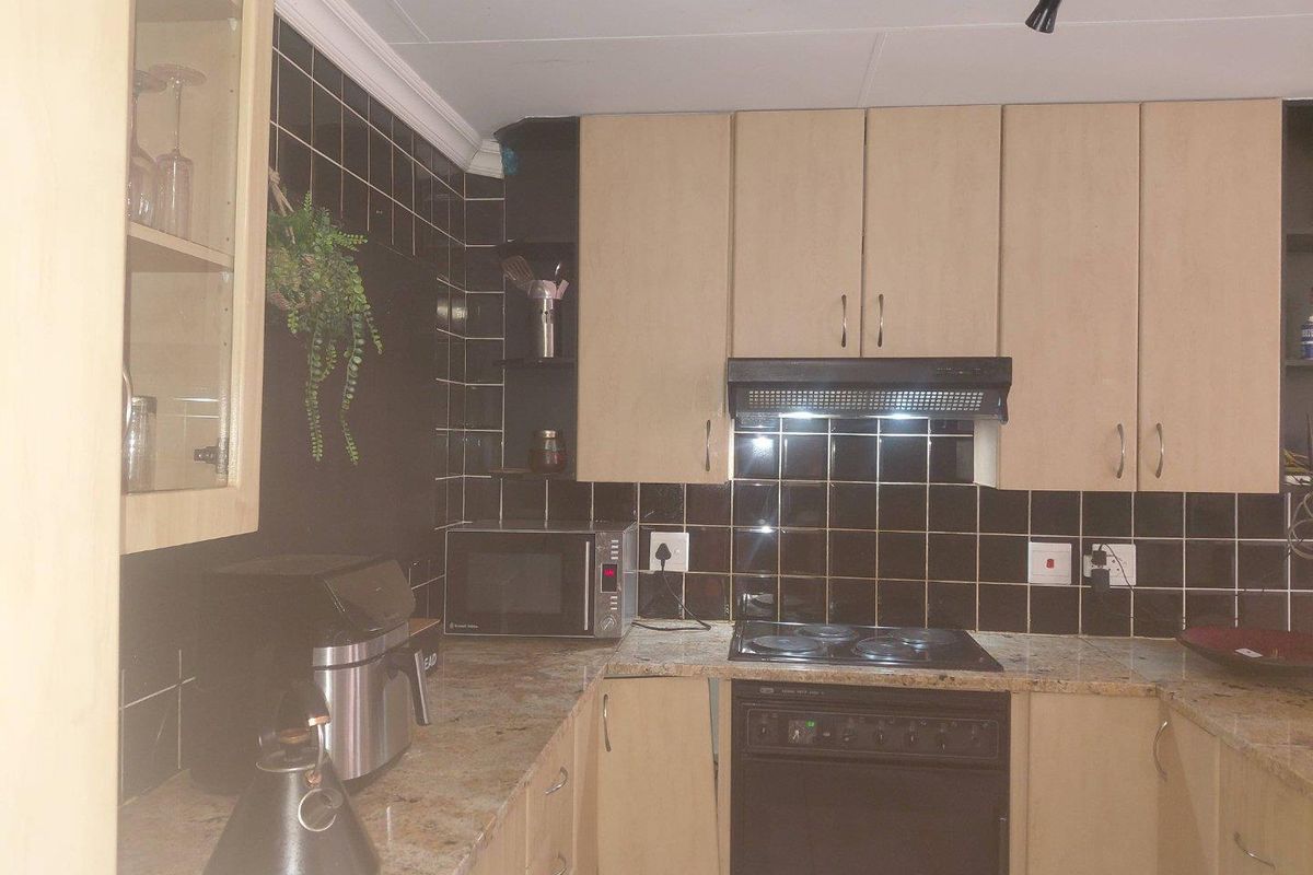 A functional kitchen featuring granite countertops, built-in cabinetry, an electric hob, and a tiled backsplash, offering a practical layout for daily meal preparation.