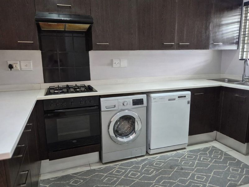 Modern kitchen featuring dark wood cabinetry, white stone countertops, built-in gas hob, oven, extractor fan, and a stainless steel sink with mixer tap.