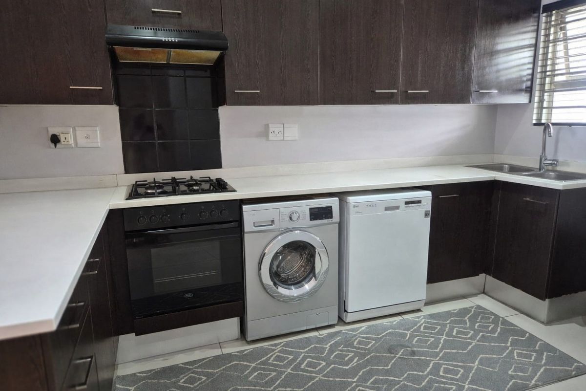 Modern kitchen featuring dark wood cabinetry, white stone countertops, built-in gas hob, oven, extractor fan, and a stainless steel sink with mixer tap.
