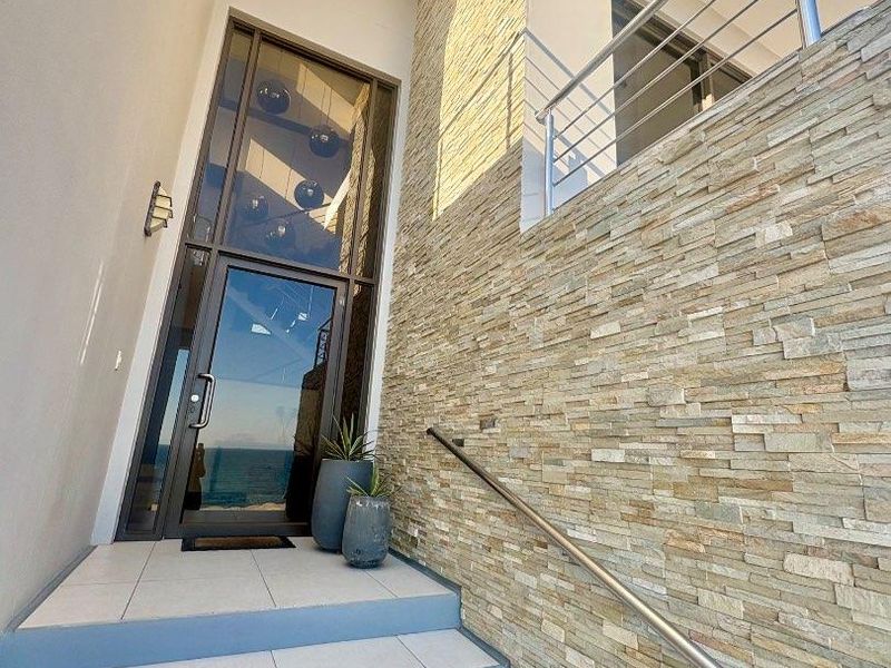 Modern entrance featuring stacked stone feature wall, tiled steps, stainless steel handrails, and a tall glass front door.