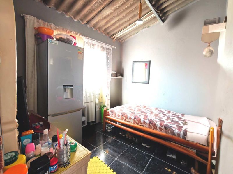 A compact bedroom featuring dark tiled flooring and an exposed corrugated roof structure, offering a functional space with potential for aesthetic improvement.