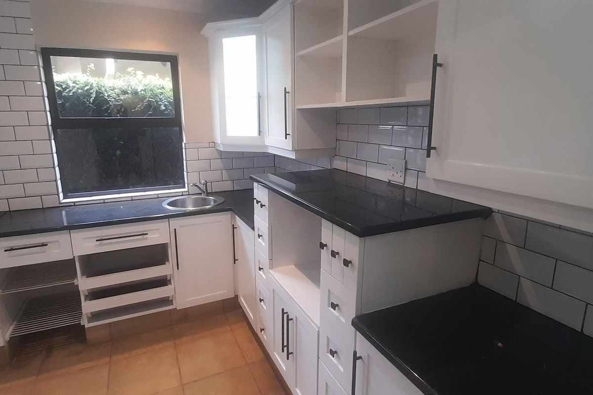 Modern kitchen featuring white cabinetry, black countertops, subway tile backsplash, stainless steel oven, and extractor fan.