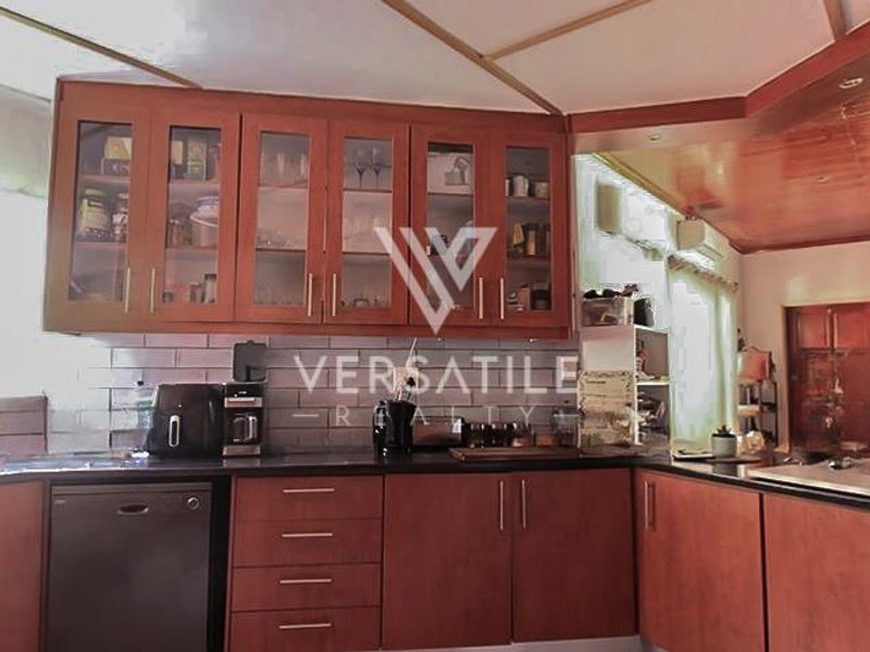 A functional kitchen featuring warm-toned wooden cabinetry, glass-fronted display units, subway tile backsplash, and dark stone countertops with integrated dishwasher.