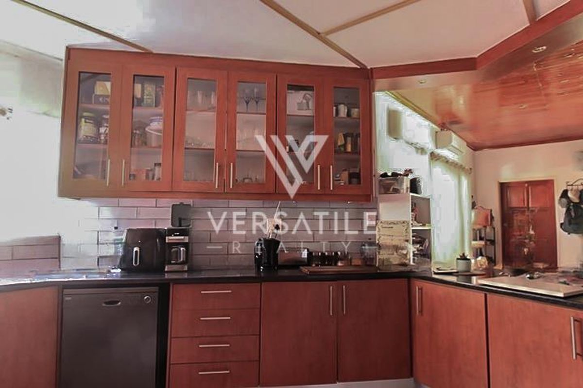 A functional kitchen featuring warm-toned wooden cabinetry, glass-fronted display units, subway tile backsplash, and dark stone countertops with integrated dishwasher.