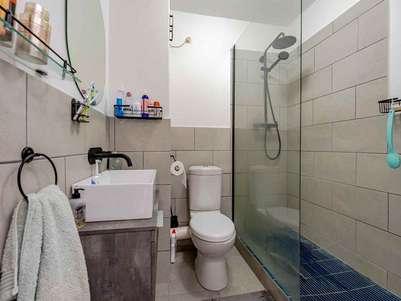 Modern bathroom featuring a vessel sink with wall-mounted tap, a glass-enclosed shower with rain head, and neutral ceramic wall tiling.