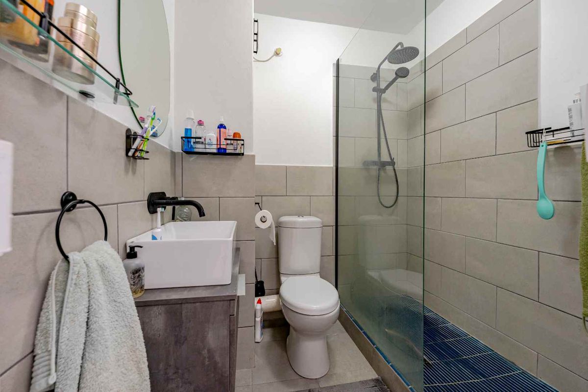 Modern bathroom featuring a vessel sink with wall-mounted tap, a glass-enclosed shower with rain head, and neutral ceramic wall tiling.