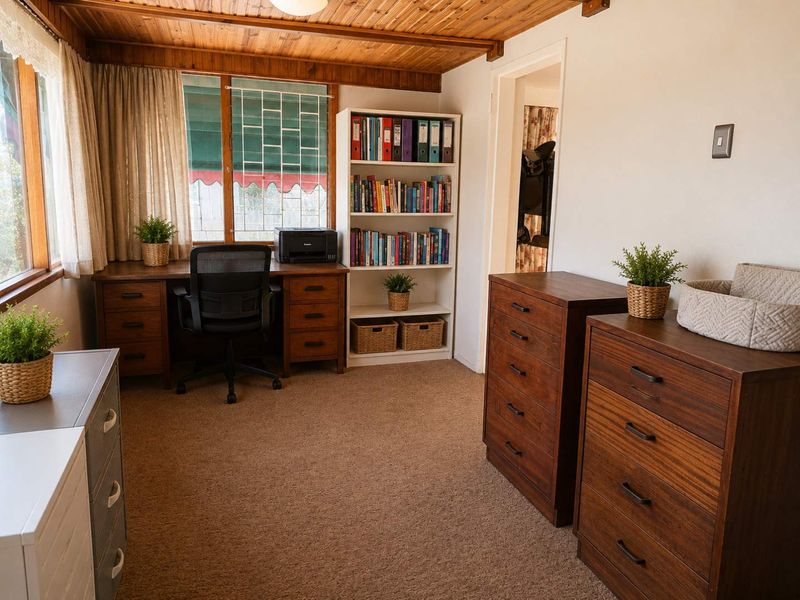 A functional home office featuring a timber-clad ceiling and large windows with security bars, providing a bright and practical workspace.