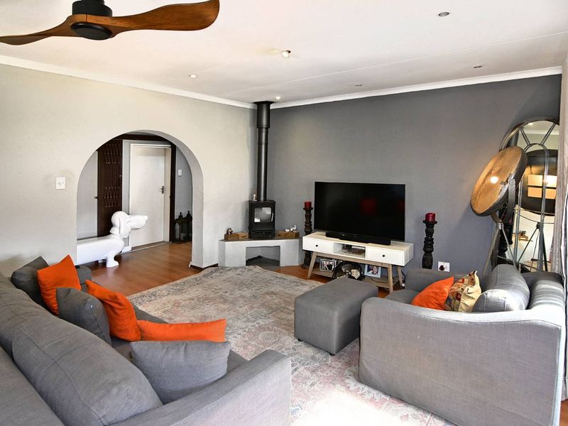 A comfortable living room featuring a wood-burning fireplace, a ceiling fan, and a distinctive architectural archway leading to an adjacent space.