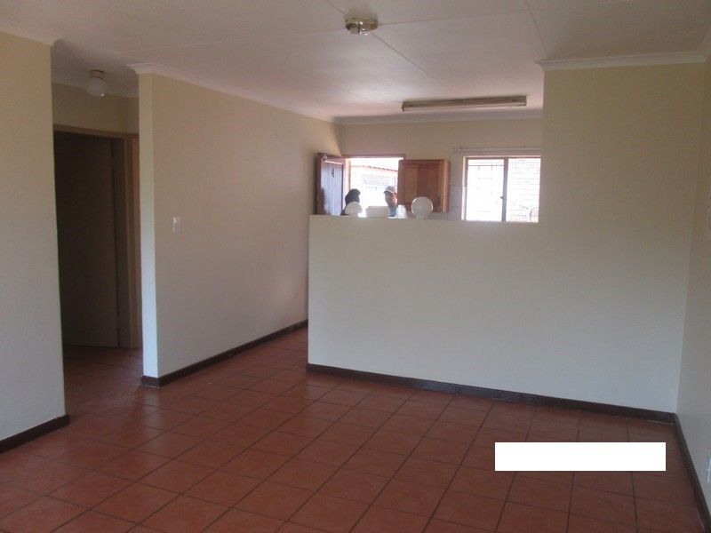 An open-plan living area featuring terracotta floor tiles and a pass-through window connecting to the kitchen space.