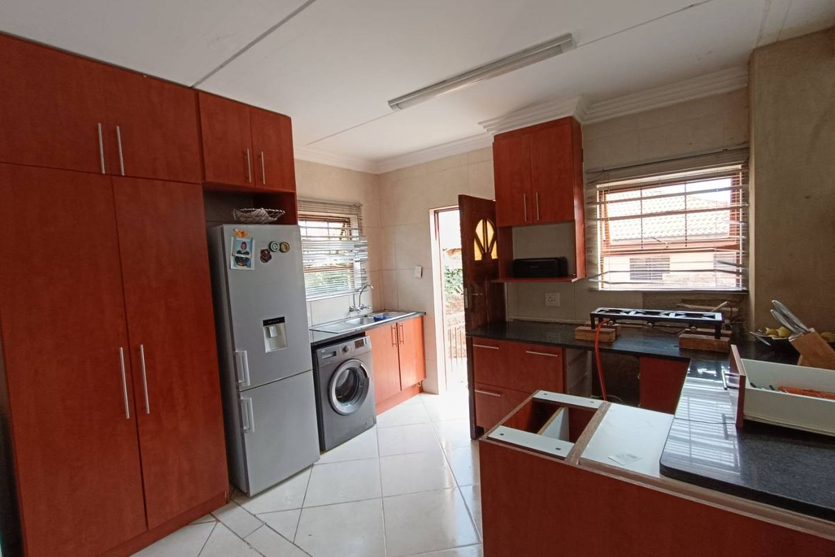 A kitchen featuring wood-finish cabinetry, dark countertops, and tiled flooring, currently requiring minor repairs to cabinetry and wall finishes.