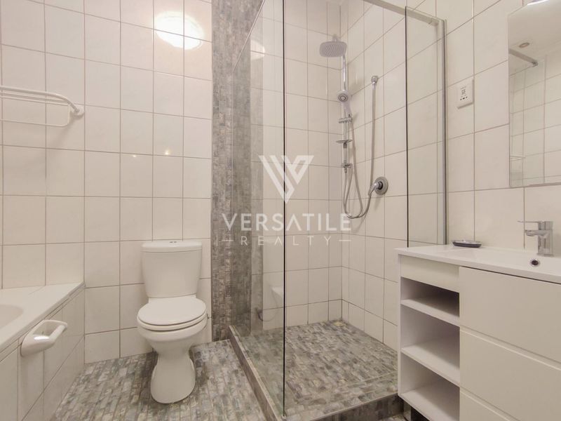 Modern bathroom featuring a glass-enclosed shower with a rain shower head, a vanity unit with basin, and neutral wall tiling.