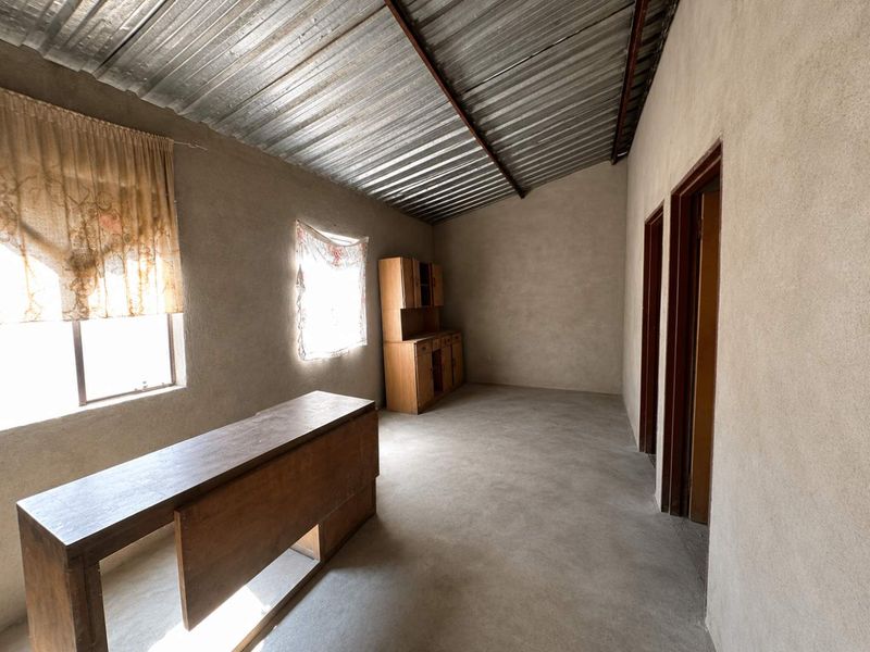 An unfinished interior space featuring exposed plaster walls, a corrugated metal ceiling, and cement flooring, offering a blank canvas for renovation.