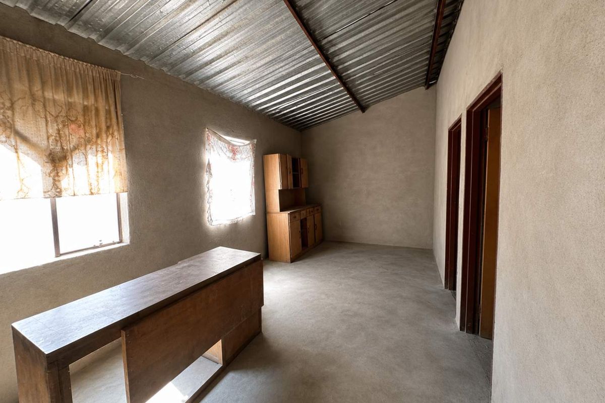 An unfinished interior space featuring exposed plaster walls, a corrugated metal ceiling, and cement flooring, offering a blank canvas for renovation.