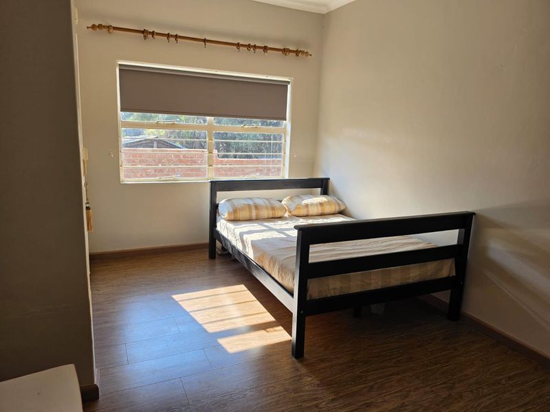 A simple bedroom featuring laminate flooring, a window with a roller blind, and a curtain rod, offering a neutral space ready for personalization.
