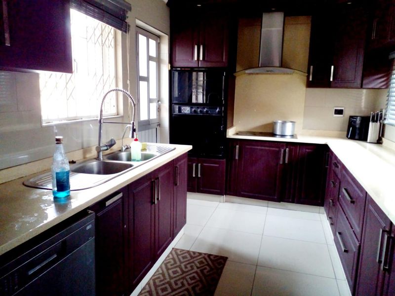 A functional kitchen featuring dark wood cabinetry, stone countertops, a stainless steel double sink, and built-in appliances including an oven and extractor fan.