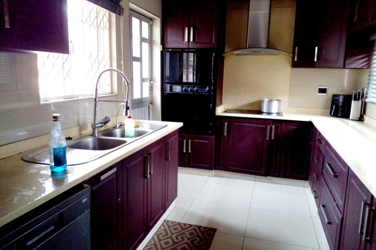 A functional kitchen featuring dark wood cabinetry, stone countertops, a stainless steel double sink, and built-in appliances including an oven and extractor fan.