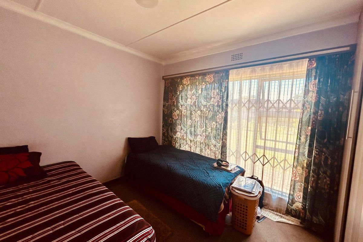 A functional bedroom featuring carpeted flooring, a large window with security gate, and built-in cupboard space.