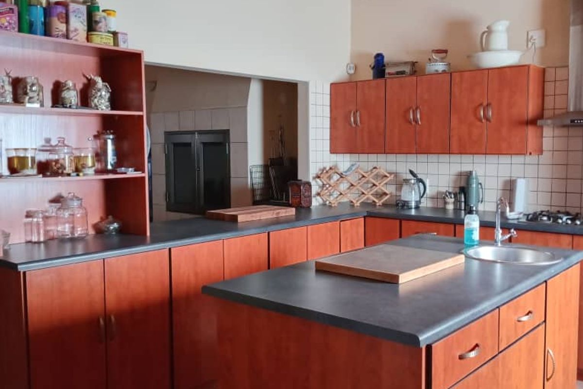 A spacious kitchen featuring wooden cabinetry, a central island with a sink, tiled backsplash, and exposed timber ceiling beams.